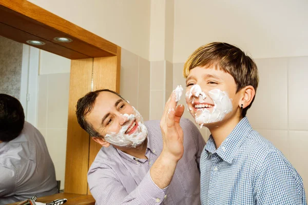ティーンエイジャーの父のフォームフェイスと彼の手は 最初の剃りのために準備し 一緒に浴室で微笑んで — ストック写真