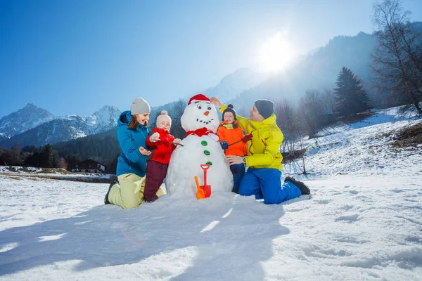 快乐的妈妈爸爸和两个小男孩和女孩一起在山上堆雪人 — 图库照片