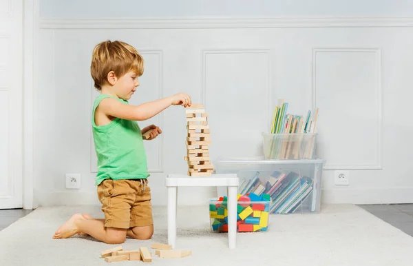 小男孩在客厅的地毯上建了一座塔 上面放着延加木块 上面放着几箱玩具和书籍 — 图库照片