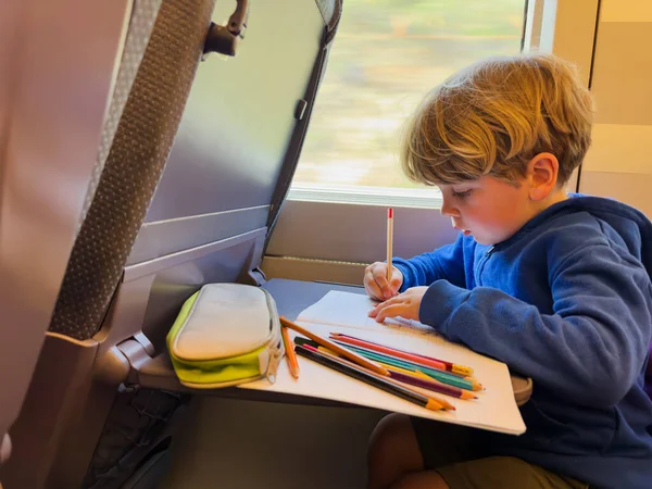 小さな男の子は 高速列車の書き込みとノートパッドでスケッチの内部の窓に座っています — ストック写真