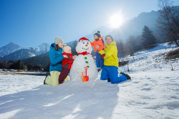 快乐的爸爸妈妈和两个小孩 男孩和女孩一起在山上堆雪人 — 图库照片