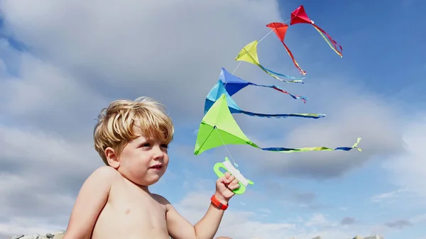 一个小男孩的特写站在那里 手里牵着许多风筝 从后面向蓝天的景色微笑 — 图库照片
