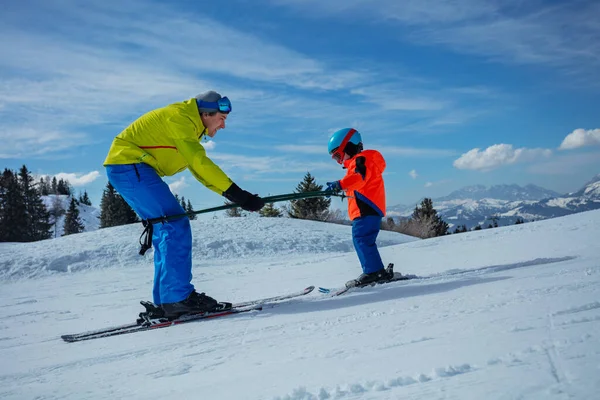 滑雪学校的老师向后滑行 教小孩滑雪板 一起滑下坡时抱住杆子 — 图库照片