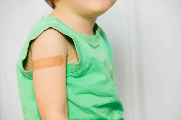 Close-up of a handsome young boy with band-aid patch on his shoulder in green shirt