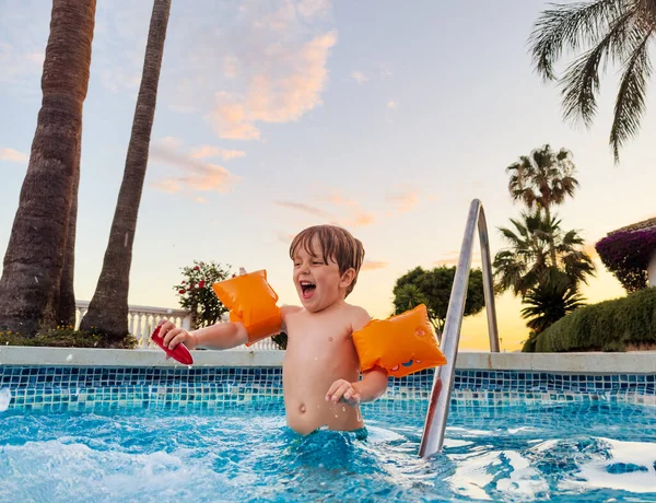 欢快的男孩在臂弯里享受日落游泳池的乐趣 欢笑着 飞溅着 — 图库照片