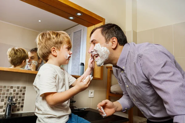 Funny family moments small kid foaming daddy face smiling in morning bathroom