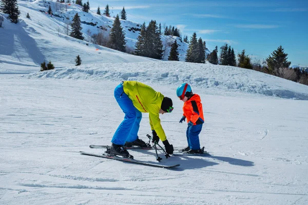 インストラクターは子供の前に滑りながら雪の動きを学ぶために手でスキーを握ることによってアルペンスロープでスキーする小さな少年を教えます — ストック写真