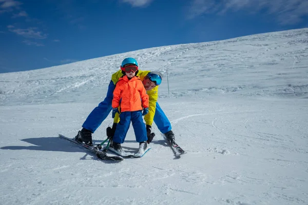 大人は雪だるまの動きを示す手でスキーバインディングを保持している後ろの小さな子供のスキーグライディングを教えます — ストック写真
