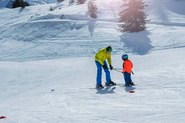 パパは後ろをグライドし 小さな子供にポールを保持して下り坂に行くスキーを教えます — ストック写真