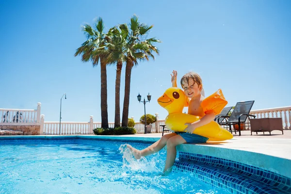 男孩穿着小鸭浮标和胳膊在水里飞溅 坐在游泳池边 在度假胜地享受炎热的夏天 — 图库照片