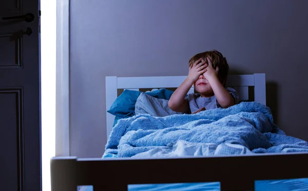Little boy sit in bed closing eyes - concept of children fears in bedroom