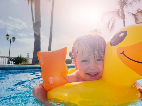 穿着小鸭浮标和花的男孩喜欢在阳光灿烂的背景下嬉笑游泳池 — 图库照片