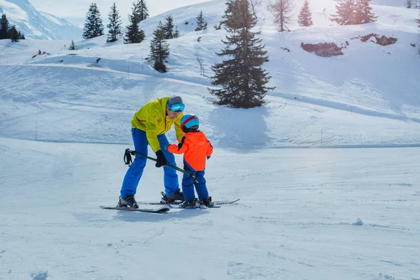 スキー学校のパパは 後ろ向きに小さな子供にポールを保持して下り坂に行くスキーを教える — ストック写真