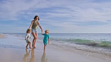 Anne ve iki küçük çocuk, kız deniz kumsalında yürüyor yaz tatilinde dalgalarla oynuyor.