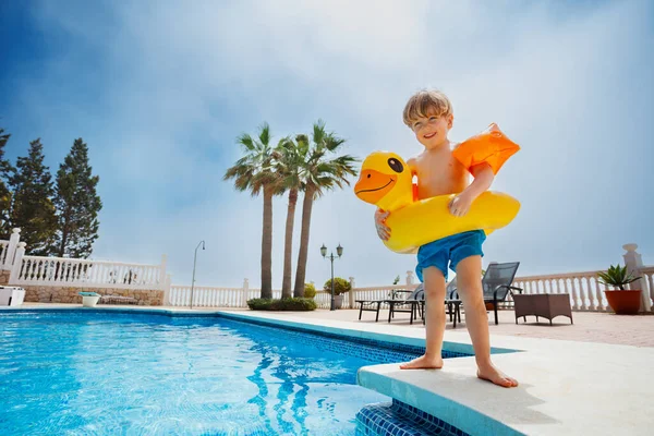 快乐的男孩 身披小鸭形状的浮标和充气的胳膊 站在游泳池边准备跳水 — 图库照片