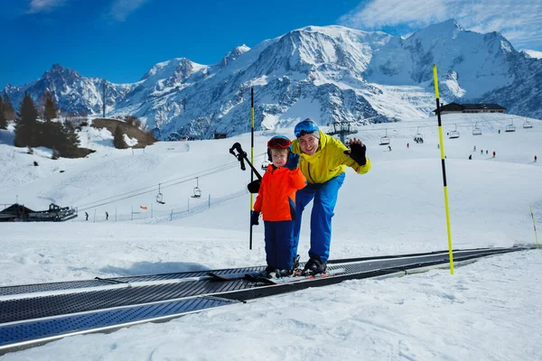 リトルボーイと父親は スキー場でスキー場を移動するウォーキングウェイベルトに乗り 脇を見下ろして手を振る — ストック写真