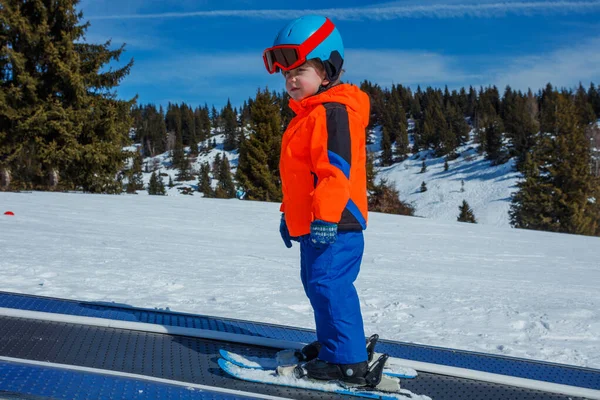 冬のプロフィールビューでスキースクールでスキーを移動する歩道ベルト上のマスクとヘルメットを持つ小さな男の子 — ストック写真