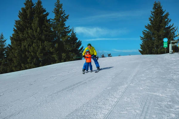 お父さんはスキーポールを保持している後ろの小さな子供のスキーグライダーを教え スノープラウのウェッジの動きを示す手と一緒に — ストック写真