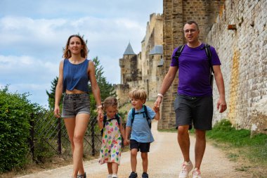 İki çocuklu mutlu bir aile yaz tatili için Carcassonne şehrini ziyaret ediyor, büyük taş duvarlar boyunca yürüyor, tarihi yerlerin tadını çıkarıyor.