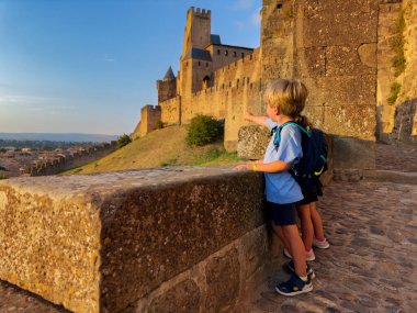 Yaz gezisindeki küçük gezginler gün batımında Fransa 'nın Occitania kentindeki ünlü Carcassonne Fransız Ortaçağ şatosunu gezerken manzaranın keyfini çıkarıyorlar.