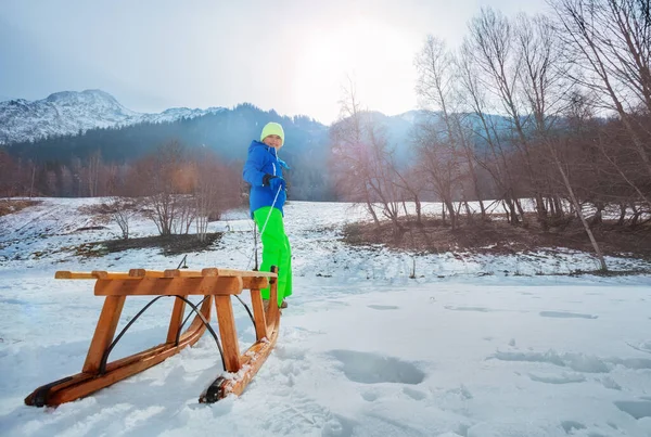 Chłopiec Stroju Zimowym Wyciągnąć Drewniane Sanie Pod Górę Obracając Patrząc — Zdjęcie stockowe