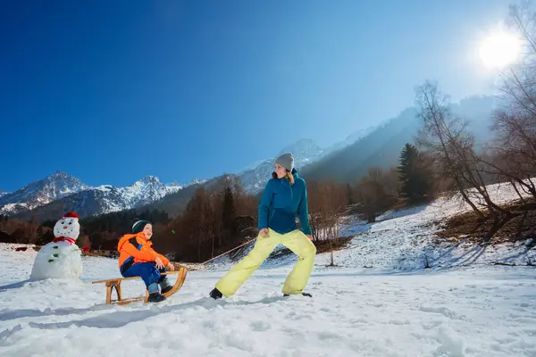 图片说明冬天 一位母亲站在高山上 把一个上坡的孩子拖到木制的雪橇上 回头看 — 图库照片