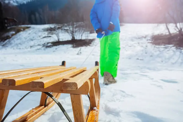 一个男孩子拉着木结构的雪橇特写爬上了积雪覆盖的高山 孩子们 — 图库照片