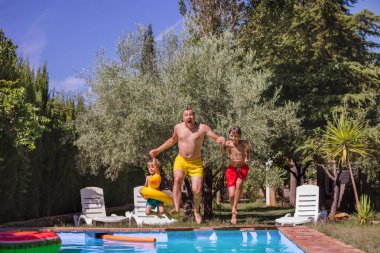 Havuz kenarında güneşli bir günde aile, birlikte suya atlamaya hazırlanıyor ve sakin bir yaz aktivitesinin tadını çıkarıyor.