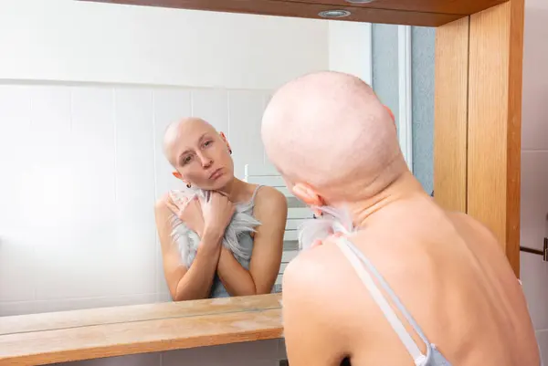 一个秃头的年轻女人在镜子里拿着一根替代的头发时 陷入了沉思 — 图库照片
