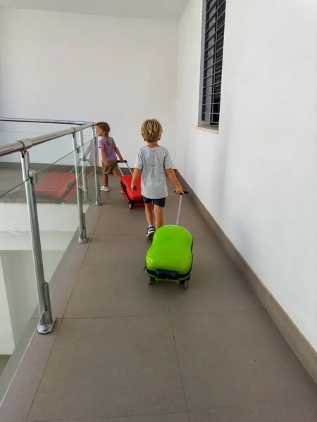 Cute little tourists, girl and boy, walk through hotel corridor with baggage in Spain, ready to check out continue their journey