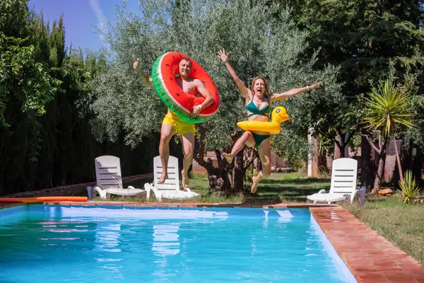 Two happy swimmers woman and man have fun at pool party dive into, using bright swim rings at summer hot day