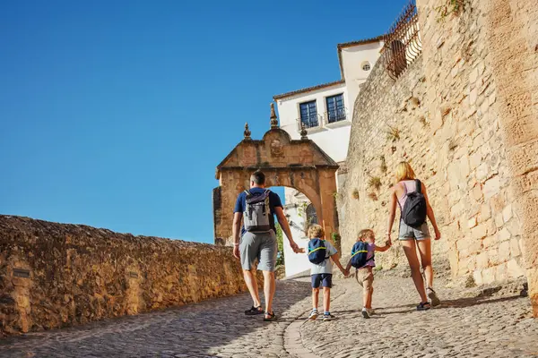 ロンダの古い部分を歩く2人の子供を持つ観光客の家族は アルコ フェリペ5世に向かい スペイン南部の夏休みを楽しんで 背後から眺める ストック画像