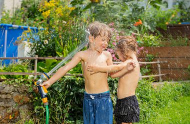 Gülen çocuklar, neşeli bir şekilde güneşli bir arka bahçede bahçe hortumu kullanırken sırılsıklam olurlar. Yaz eğlencesi aktiviteleri.