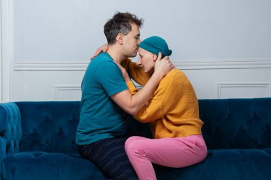 İki birey teselli edici bir kucaklaşmayla, adam kanser karısını oturma odasında öpüyor.