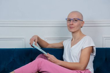 Kel bir kadın, evdeki tableti incelerken mavi kadife koltukta uzanan gözlükleriyle kanserle mücadele ediyor.