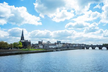 Meuse nehrine bakan tarihi bir kilise kulesi ve parçalı bulutlu bir gökyüzünün altında taş bir köprüsü olan Avrupa 'nın tuhaf bir kasabası Maastricht manzarası.