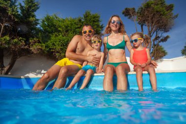 Dört kişilik neşeli bir grup, iki yetişkin ve çocuk, aydınlık yaz gününde bir havuz partisinde eğleniyorlar.