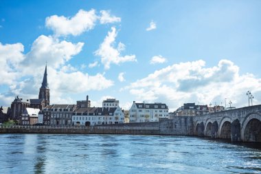 Resimli Maastricht nehir kenarı antik bir kemerli Sint Servaas köprüsü, antika bir kasaba ve seçkin bir kilise kulesi.