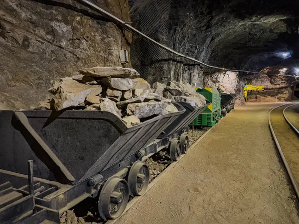 Loş bir yeraltı madencilik tünelinde raylarla dolu metal bir maden arabası.