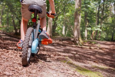 Genç bir bisikletçi ormanlık patika boyunca pedal çeviriyor, bacakları ve tekerlekleri alçak açıdan görüyor, yaz tatilleri kavramı