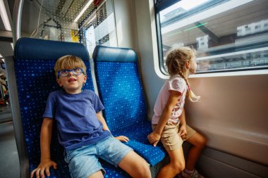 Bir çift çocuk trenin içinde oturur, kız pencereden dışarı bakar oğlan ise merakla bekler.