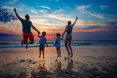 Dört çocuklu neşeli bir aile, iki ebeveyn, erkek ve kız alacakaranlıkta plajda birlikte zıplıyorlar, mükemmel tatiller geçiriyorlar.