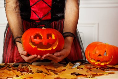 Cadı elbiseli kadın elleri Cadılar Bayramı partisine hazırlanan neşeli bir ifadeyle balkabağı sunar.