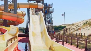 Su parkı maceracıları oğul ve baba, güneşli bir park ortamında kanarya renginde bir su kaydırağına binmenin zevkine varırlar..