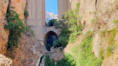 Görkemli bir taş köprü Puente Nuevo, İspanya 'nın Ronda kentindeki açık mavi gökyüzünün altında kayalık uçurumlar ve seyrek yeşilliklerle çevrili derin bir vadiyi kaplar.