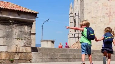 Çocuklar yaz gezilerinde sırt çantalarıyla güneşli bir günde Girona 'nın tarihi katedraline doğru adımlarını atıyorlar.