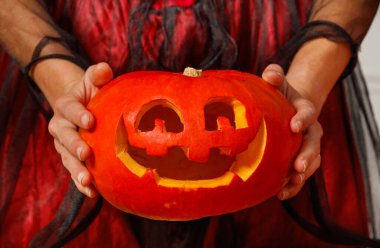 Kılık değiştirmiş insan ellerinin yakınında ürkütücü gülümseyen yüzlü oyulmuş bir balkabağı tut.