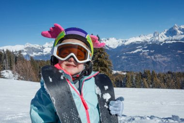 Mutlu şirin kız komik bir kask takıyor. Kanatları var. Güneşli havada, dağ yamacında eğlenmeye hazır.