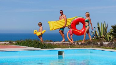 Dört kişilik bir grup, muhtemelen bir aile, havuz kenarında eğlence için hazırlar, çeşitli yüzen oyuncaklarla övünüyorlar.