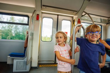 İki küçük çocuk, mavi gözlüklü bir çocuk ve pembe tişörtlü bir kız, bir direğe tutunarak bir sonraki istasyondan çıkmaya hazırlanıyorlar.